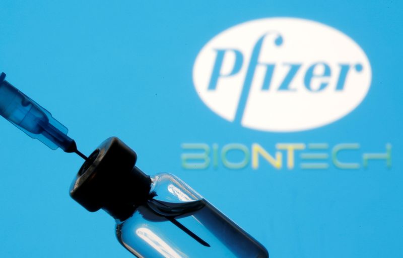 Vial and sryinge are seen in front of displayed Pfizer