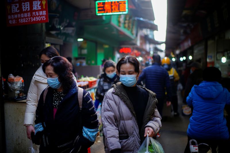 People wearing face masks walk on a street market, following