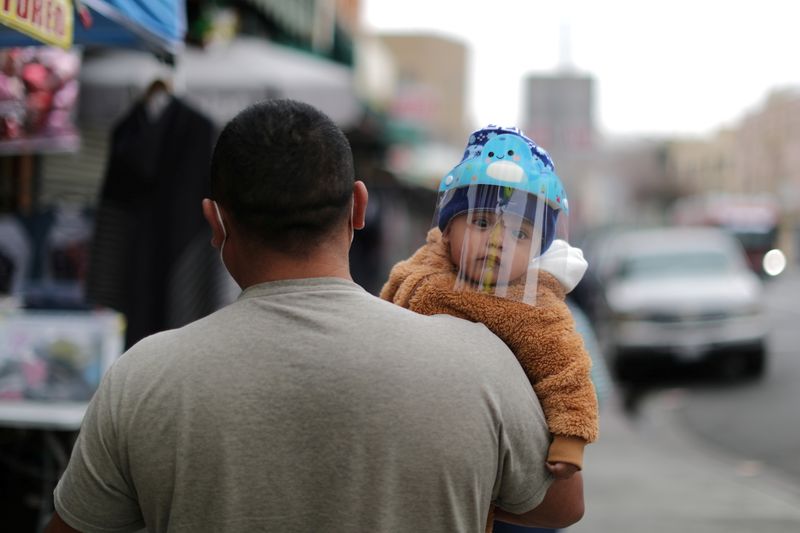 A man carries a baby wearing a mask to protect