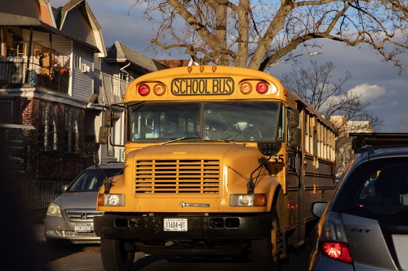 A driver wearing a protective mask drives a school bus