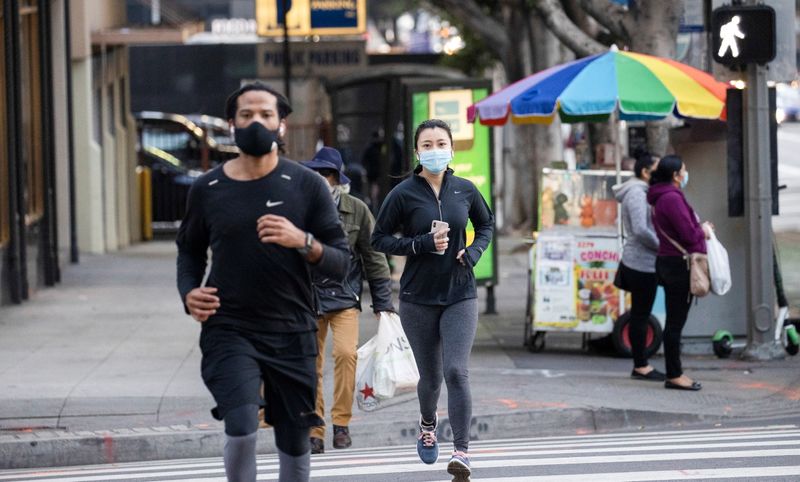 People wearing personal protective face masks jog downtown during the