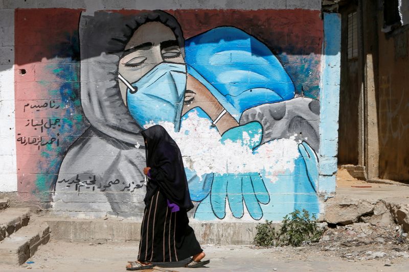 A Palestinian woman walks past a mural, amid COVID-19 outbreak,