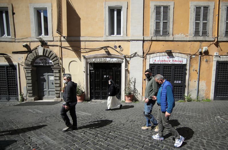 People wearing protective masks walk past closed shops in Rome
