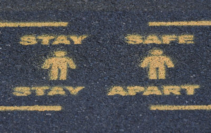 Public health signs are seen sprayed on a pavement, whilst
