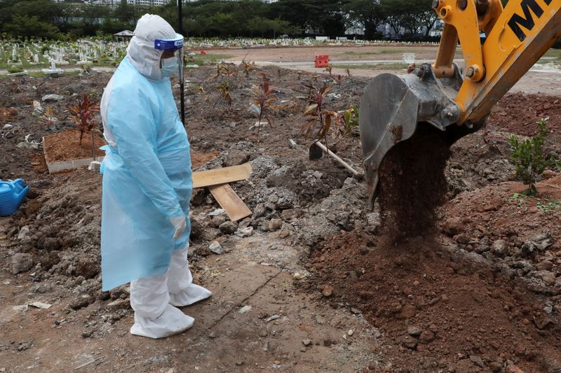 A cemetery worker wearing a protective suit helps to bury