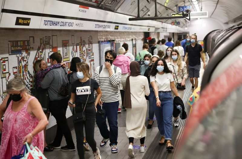People wearing protective face masks walk along a platform on