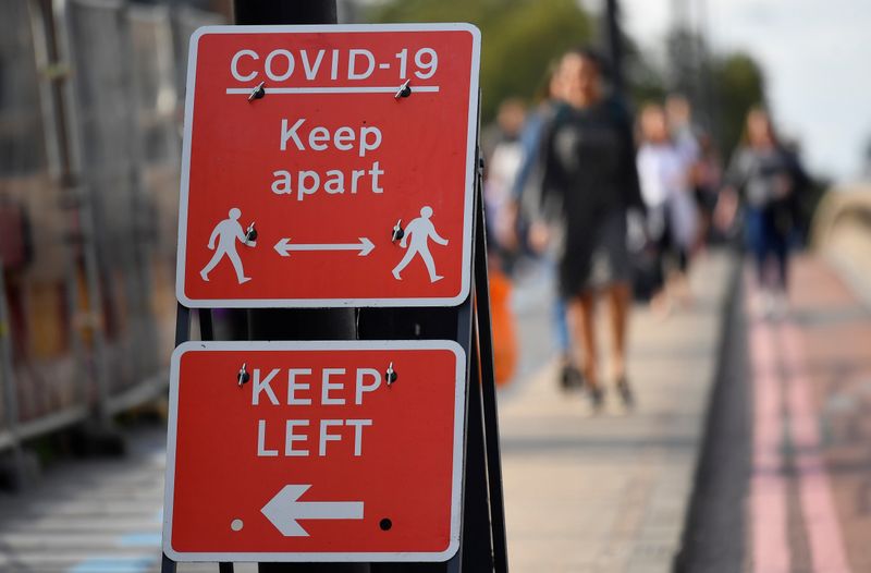 Pedestrians walk near public health signs, whilst the reproduction “R”