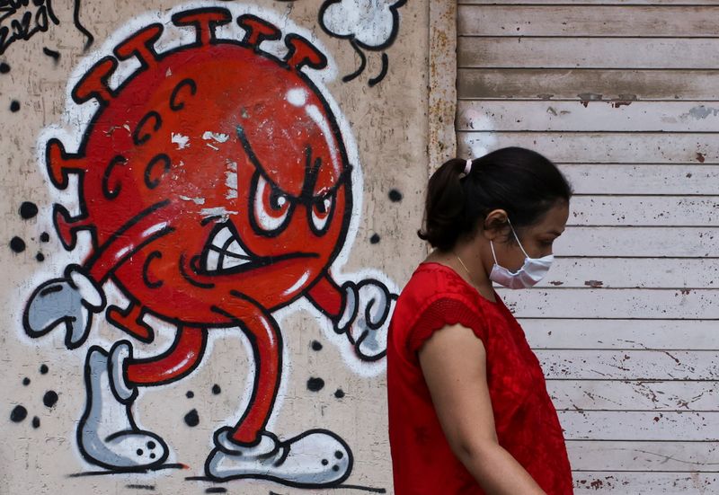 Woman walks past a coronavirus-themed graffiti on a street in