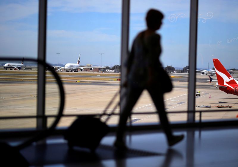 A passenger walks with their luggage towards a Qantas Airways
