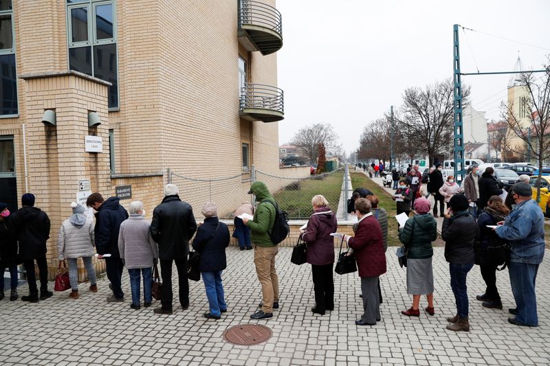 People stand in a queue for vaccination in front of