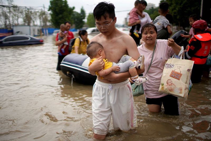FILE PHOTO: Man holding a baby wades through a flooded