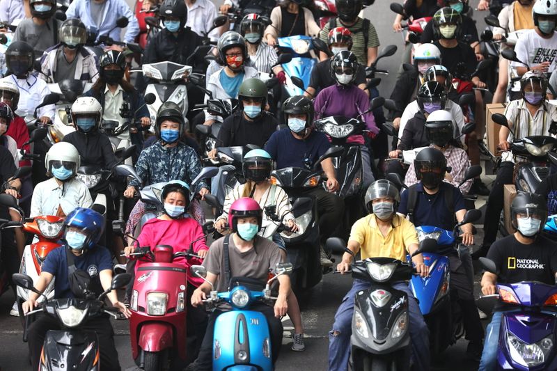 People riding motorcycles and wearing protective face masks wait at