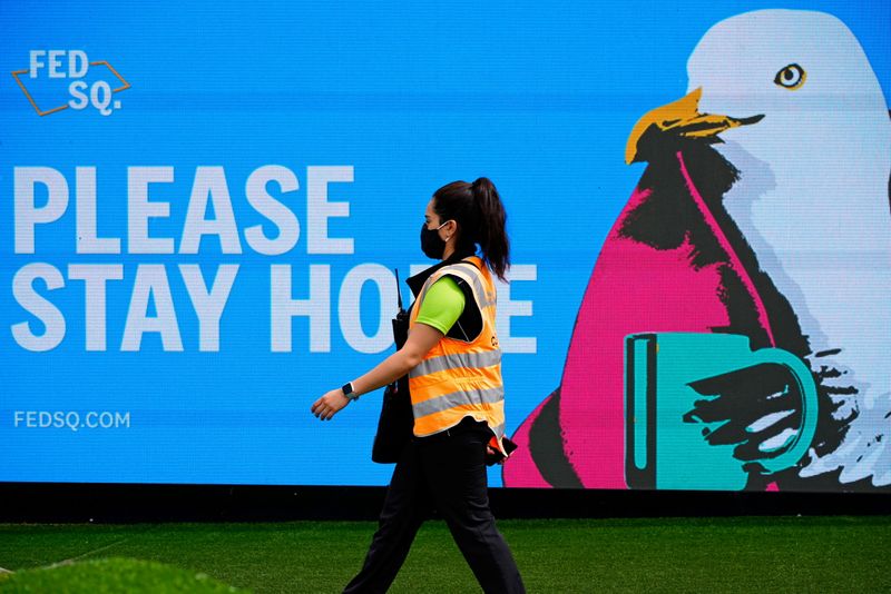 An essential worker walks past a ‘Please Stay Home’ sign