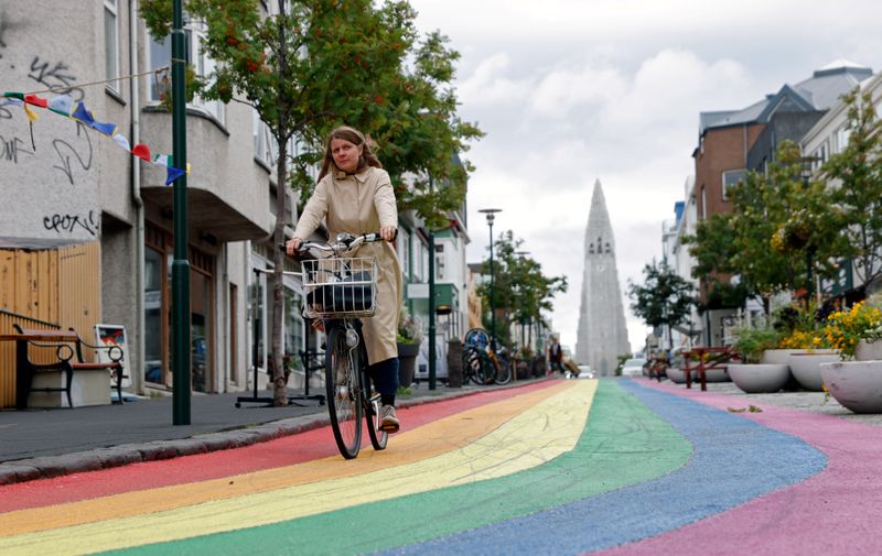 A woman cycles down a street painted in rainbow colours