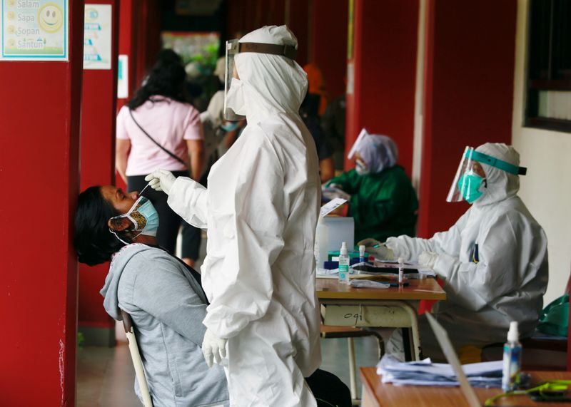 A healthcare worker in personal protective equipment takes a swab