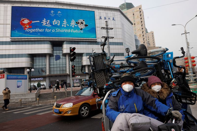 People transport sharing bikes past a billboard advertising the Beijing