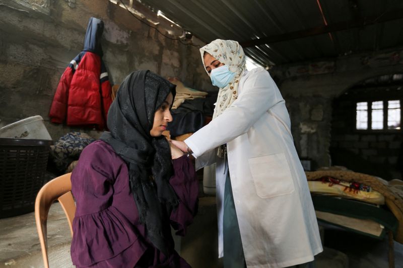 Palestinian medical worker vaccinates a Palestinian woman against the coronavirus