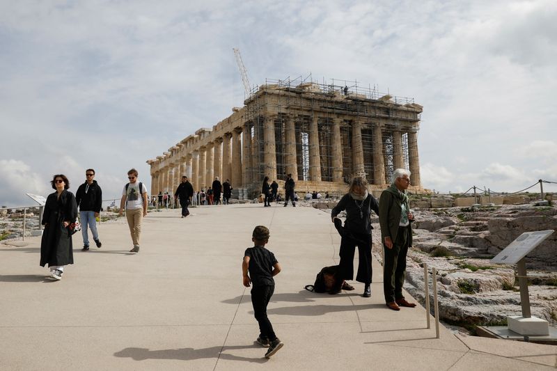 Tourists walk past the ancient Parthenon temple atop Acropolis hill