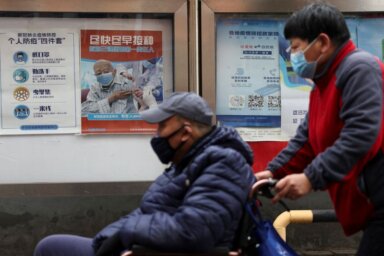 FILE PHOTO: People pass by a poster encouraging elderly people