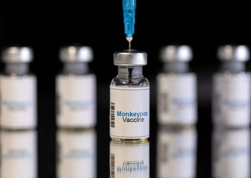 Illustration shows mock-up vials labeled “Monkeypox vaccine” and medical syringe