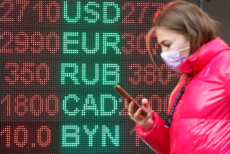 FILE PHOTO: A woman walks past a board showing currency