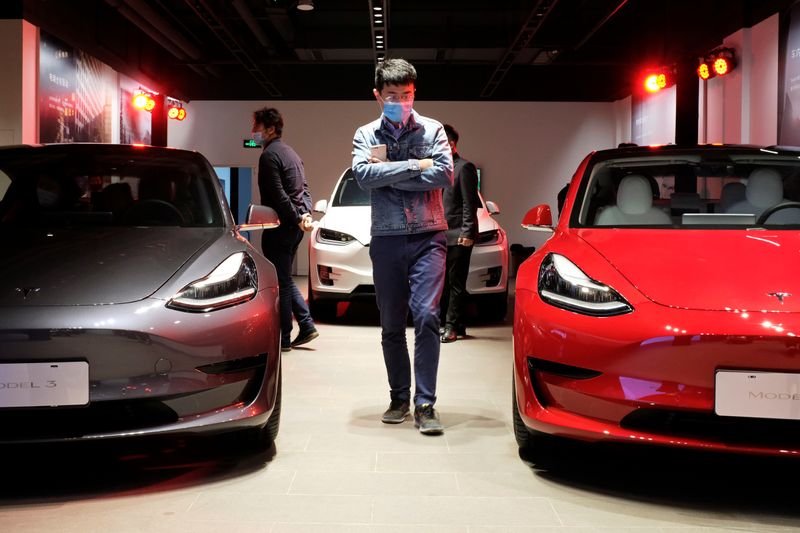 Man walks by Tesla Model 3 sedans and Tesla Model