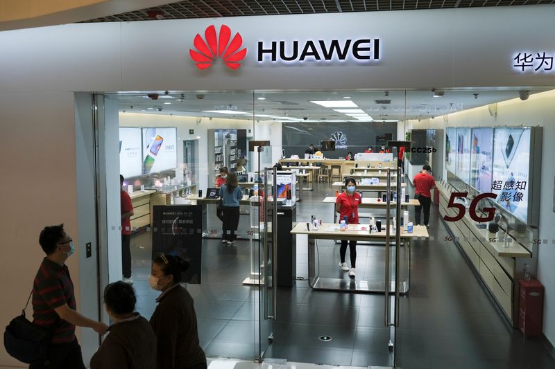 People wearing face masks walk past a Huawei store at