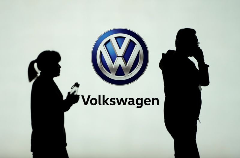 People pass in front of a Volkswagen logo ahead of