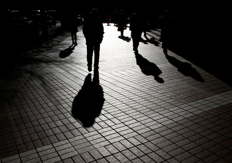 Pedestrians cast shadows as they make their way at a