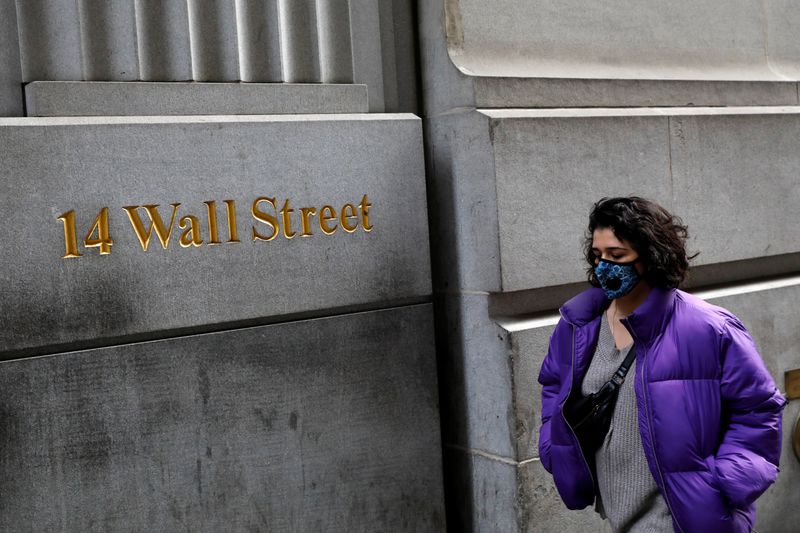 A person wearing a face mask walks along Wall Street