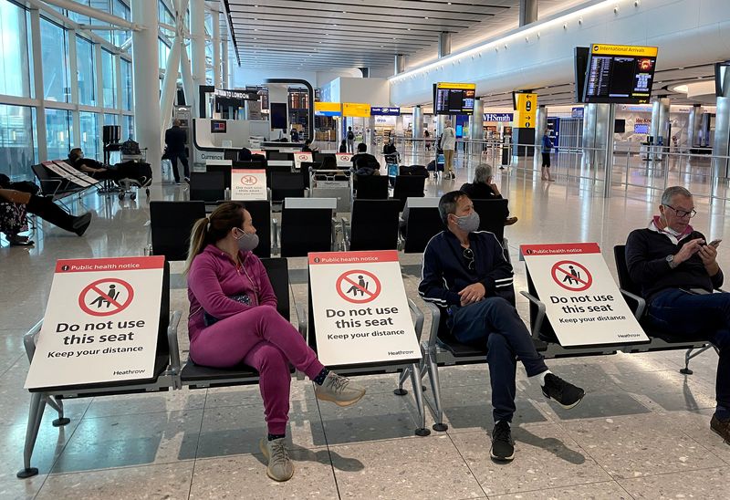 FILE PHOTO: People sit amongst socially-distanced seating signs at Heathrow