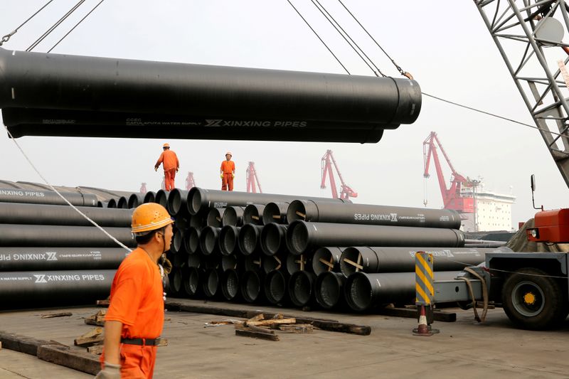 Workers direct a crane lifting ductile iron pipes for export