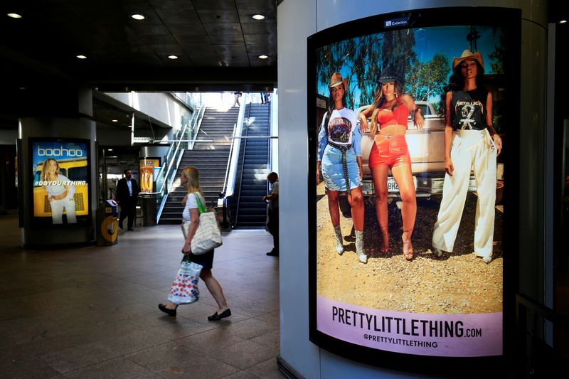 FILE PHOTO: A shopper walks pass advertising billboards for Boohoo