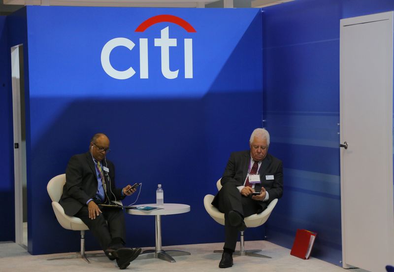 Two men look at their mobile phones under the Citigroup