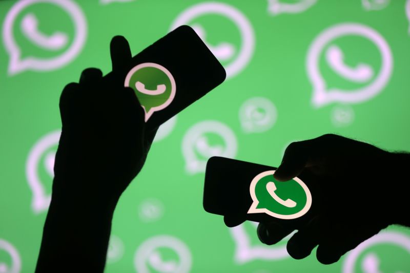 Men pose with smartphones in front of displayed Whatsapp logo