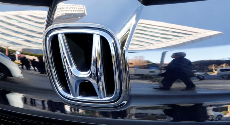 People are reflected on a Honda Motor car outside the
