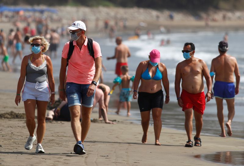 FILE PHOTO: Several people walk along the beach wearing face