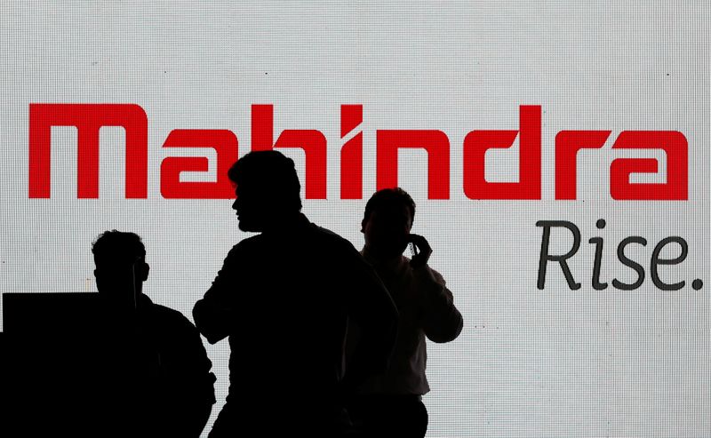 People walk past a screen displaying Mahindra and Mahindra logo