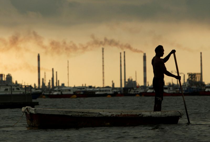 FILE PHOTO: A fisherman rows his dinghy past oil refineries