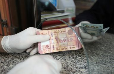 A customer wearing gloves holds Lebanese pounds at a currency