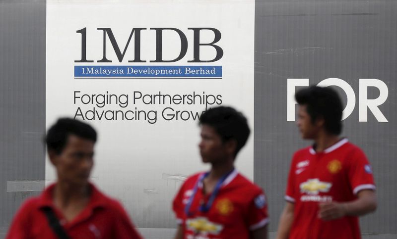 Men walk past a 1Malaysia Development Berhad (1MDB) billboard at