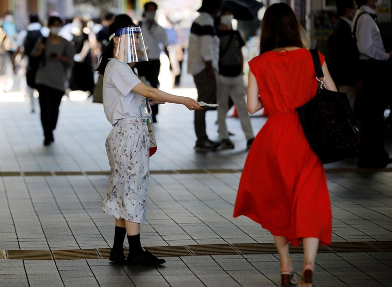 A saleswoman wearing a face shield distributes leaflets on the