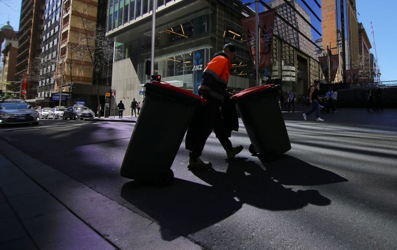 A sanitation worker walks across a street with bins
