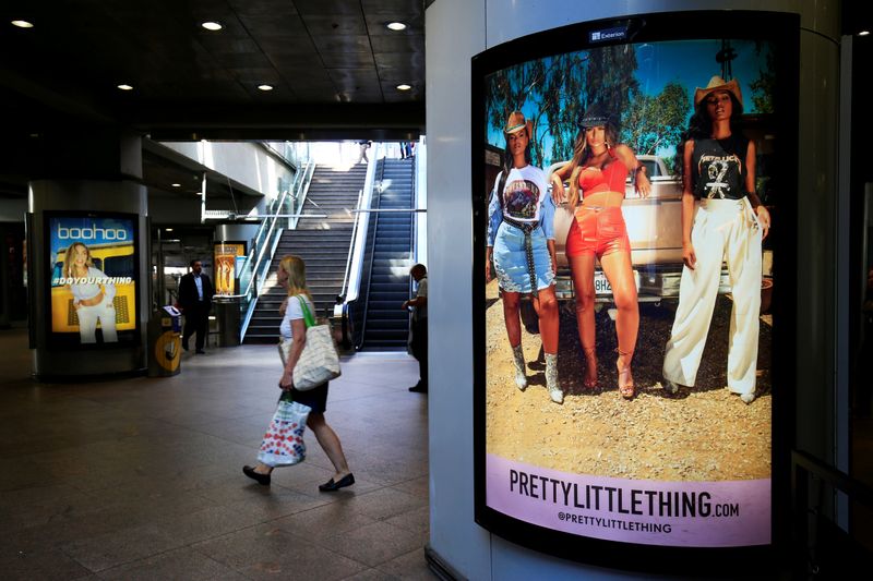 A shopper walks pass advertising billboards for Boohoo and for