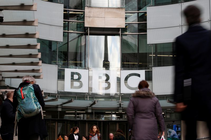 Pedestrians walk past a BBC logo at Broadcasting House, as