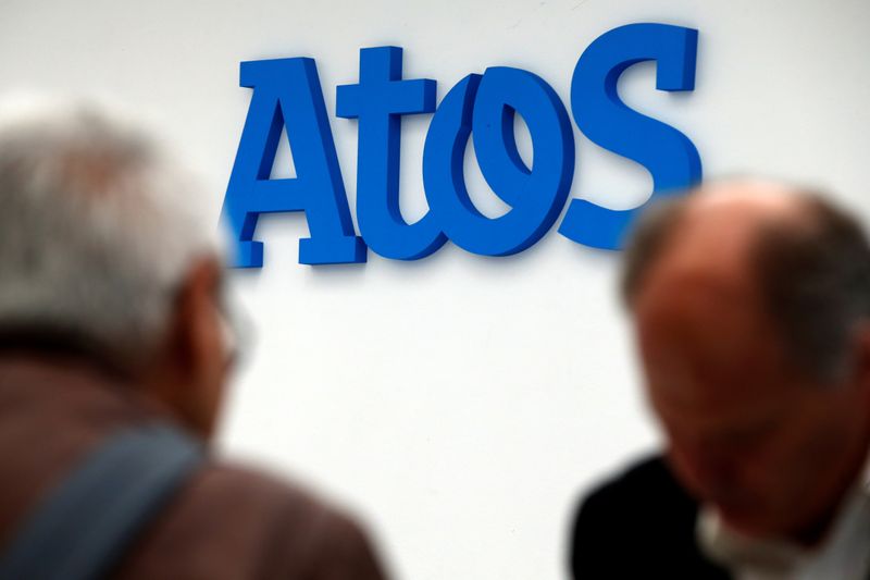 People walk in front of the Atos company’s logo during