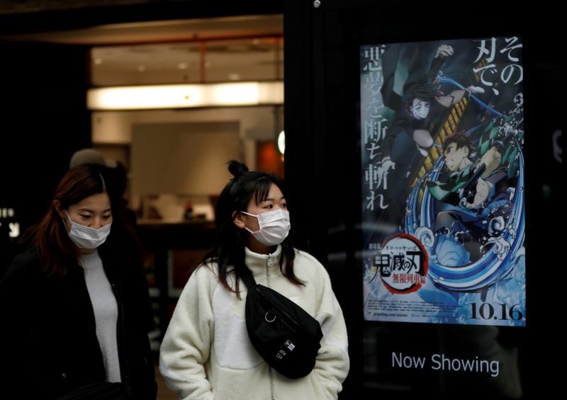 FILE PHOTO: Women masks walk past a poster for the
