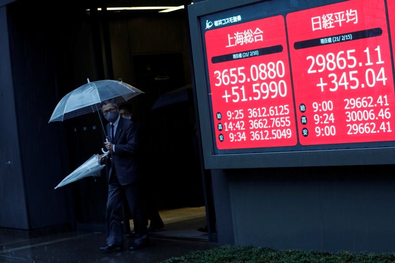 Men holding umbrellas walk near an electric board showing Nikkei