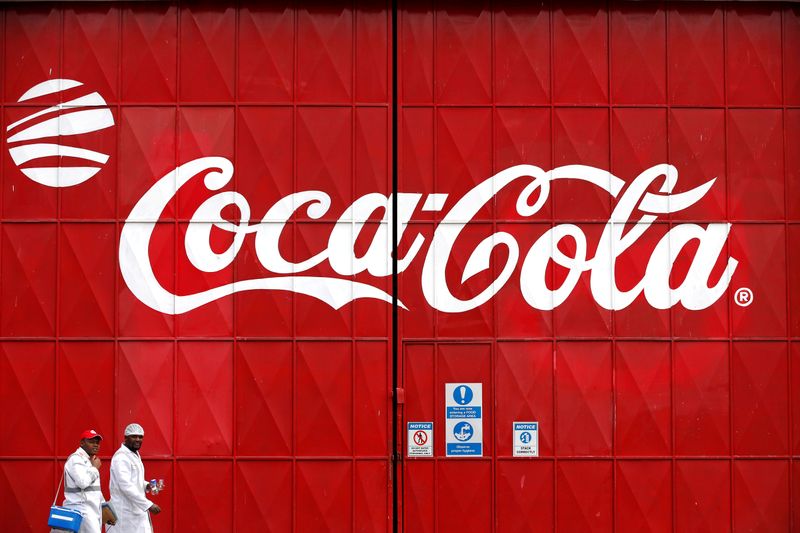 Workers walk past a Coca Cola logo painted on a