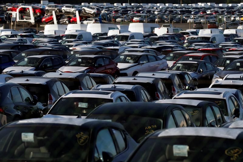 Stocks of new cars are parked in a lot, at
